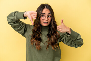 Young caucasian woman isolated on yellow background showing thumbs up and thumbs down, difficult...