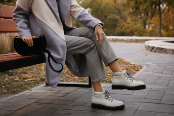 Stylish woman with trendy black baguette bag on bench in park, closeup