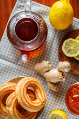 A kettle of strong infused tea on a napkin next to lemon ginger and jam and donuts with cream.