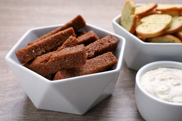 Different crispy rusks and dip sauce on wooden table, closeup