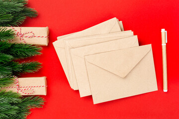 mockup blank stacks of paper craft envelopes and craft pen on red insulated background with spruce twigs and gift packages. 