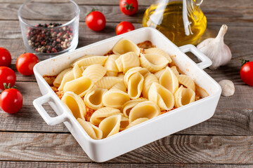 Feta cheese pasta sauce recipe step. Tomatoes drizzled with olive oil in a baking dish with a feta cheese block in the middle and sprinkled with salt and freshly ground pepper.