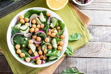 Chickpea salad with cucumber, spinach, parsley, onions and lemon in a plate on a served table, selective focus. Tasty and healthy vegetarian food,  Mediterranean cuisine. Top view. Copy space.
