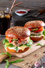 Two burgers with beef cutlet, tomato, cheese and arugula in traditional buns, served on a board with on a wooden background.