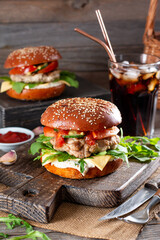 Two homemade burgers with fried cutlet, cheese, onion, tomato, cucumbers and arugula, ketchup on board stands on dark wooden table