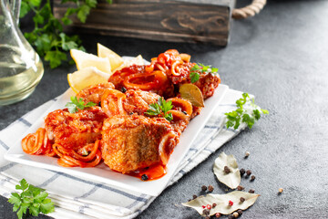 Delicious fish in tomato sauce with lemon and parsley close-up on a plate