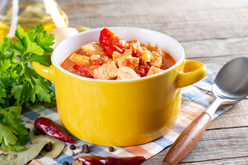 Chicken stew with paprika, onion and sour cream in plate on wooden background. Traditional Hungarian dish Paprikash.