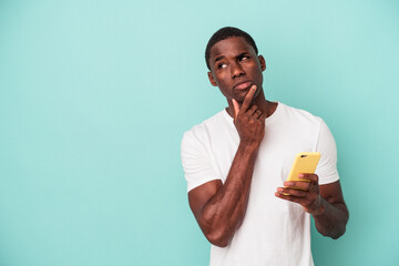 Young African American man holding a mobile phone isolated on blue background looking sideways with...