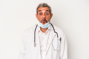 Middle age doctor man wearing a mask for virus isolated on white background  shrugs shoulders and open eyes confused.