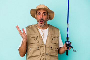 Middle age caucasian fisherman holding rod isolated on blue background  surprised and shocked.