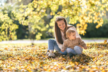 Young mother with a one-year-old toddler walking and hugging in the autumn park
