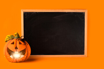 Halloween holiday concept. Jack o lantern with light bokeh, spider and blank frame chalkboard on orange background. Halloween festival party, greeting card with mockup copy space.