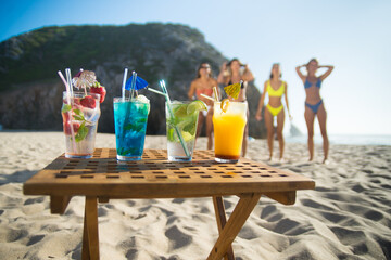 Close-up of cocktails. Multicolored fancy drinks in glasses at beach, female friends in background. Party, outdoor activity, beverages concept