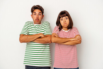 Young mixed race couple isolated on white background shrugs shoulders and open eyes confused.