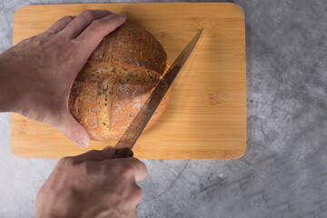 hands cutting loaf of bread on wooden cutting board