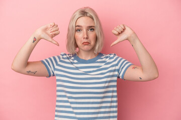 Young caucasian woman isolated on pink background showing a dislike gesture, thumbs down....