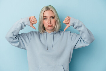 Young caucasian woman isolated on blue background showing a dislike gesture, thumbs down....
