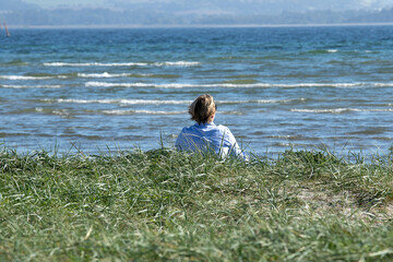 Woman sitting by the beach looking at the Sea.