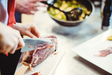 Detail shot of chef cook cutting Parma ham with a knife for use in a dish