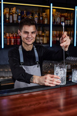 Barman stirring ice cubes in cocktail glass with spoon