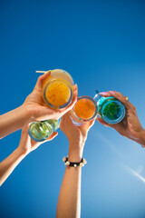 Close-up of friends clinking glasses. Multicolored fancy drinks in glasses, women clinking glasses....
