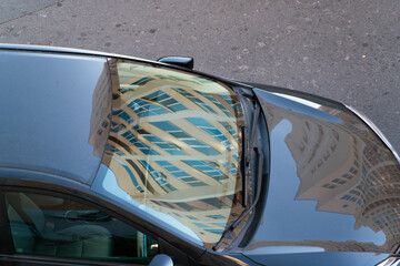 Reflections of houses on the surface of a car standing on the asphalt