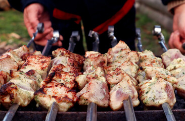 The concept of cooking a barbecue on your own in nature. Pieces of marinated pork, strung on a skewer, against the background of hands holding skewers