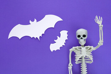 Skeleton with two white paper cut flying bats like blank speech bubbles on purple Halloween...