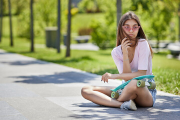 beautiful skateboarder girl with skateboard sitting outdoors