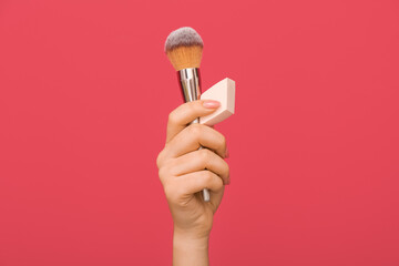 Female hand with stylish makeup sponge and brush on color background