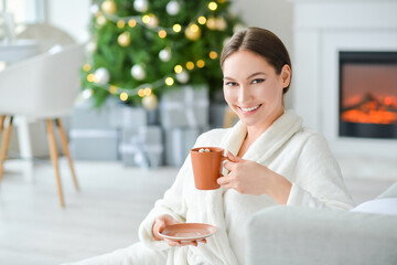 Beautiful young woman with cup of hot cacao drink at home on Christmas eve