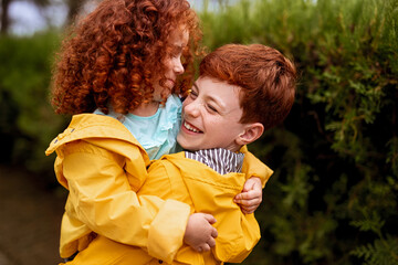 Brother and sister in yellow raincoats embracing