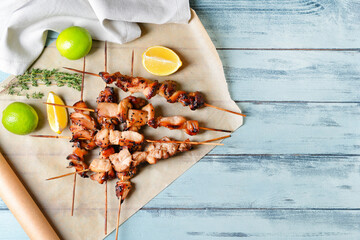 Parchment with grilled chicken skewers on color wooden background