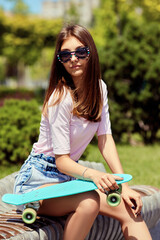 beautiful skateboarder girl with skateboard sitting outdoors