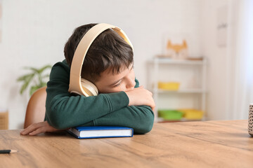 Little boy with book and headphones sleeping at table
