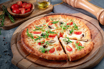 Pizza with mushrooms, cherry tomatoes, arugula and cheese on a wooden round board. Italian pizza funghi