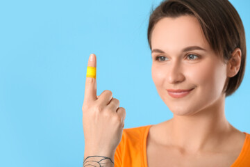 Young woman with plaster onto her index finger on blue background