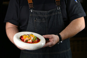 chef hold ceramic plate with salmon tartar on black background