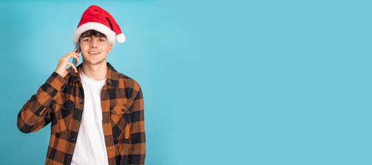 portrait of teenage boy talking on mobile phone wearing santa claus hat isolated on blue background
