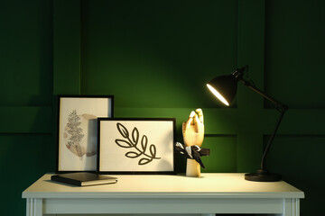 Table with frames, wooden hand and glowing lamp in dark room