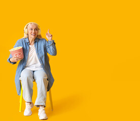 Fototapeta premium Mature woman with tasty popcorn pointing at something on color background