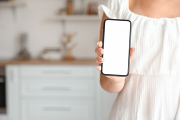 Young fashionable woman holding mobile phone in room, closeup