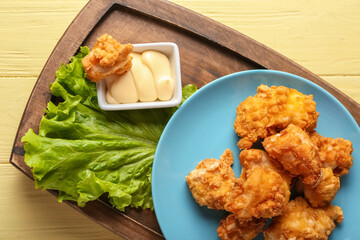Board with tasty fried popcorn chicken and sauce on color wooden background