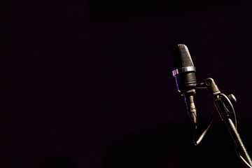An XLR microphone with an attached black cable on a black mic stand against a dark background
