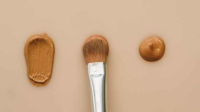 Smearing foundation tones on beige background. Brown cream texture close-up, using brush. Makeup and beauty products concept, cosmetics, eyeshadow palette, bronzer or concealer.