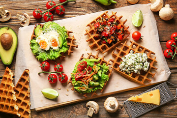Board with delicious Belgian waffles and vegetables on wooden background