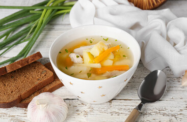 Bowl of delicious dumpling soup and bread on light wooden background