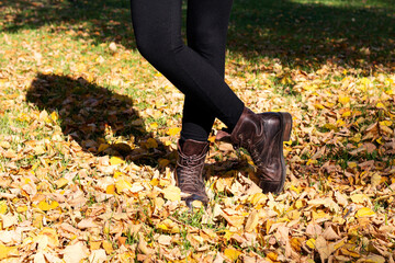 Woman's legs in brown boots in autumn foliage