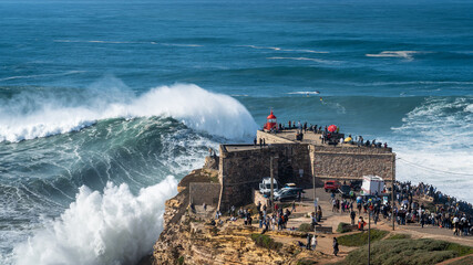 Giant waves breaking near the historic Fort of Sao Miguel Arcanjo Lighthouse in Nazare, Portugal....