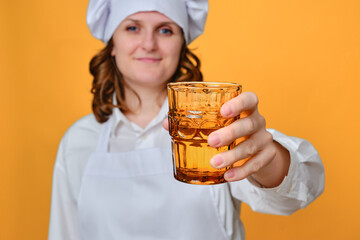 Woman chef holding a glass of water on a yellow studio background